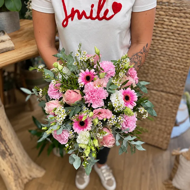 Bouquet de gerberas roses, roses et gypsophile tenu par une fleuriste