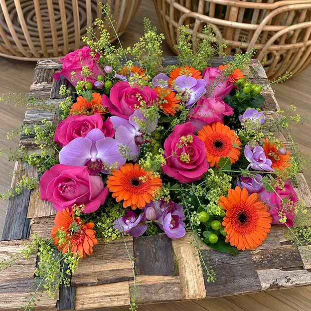 Coussin funéraire de roses fuchsia, gerberas orange et orchidées sur une palette de bois