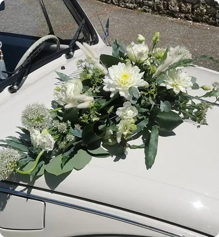 Composition florale blanche posée sur le capot d’une voiture de mariage