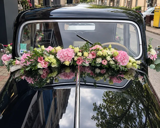 Voiture des mariés décorée d’une composition de roses roses sur le capot