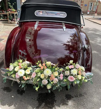 Voiture ancienne bordeaux décorée d’une composition florale de mariage